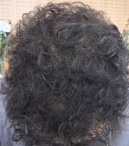 Close do topo de cabelo escuro e cacheado com a região da coroa visível.