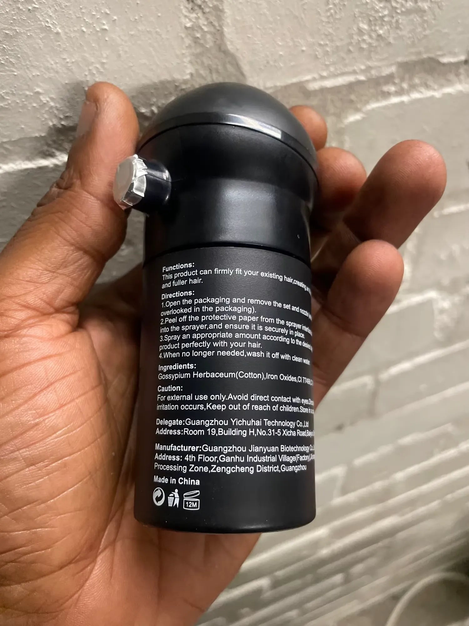 Um frasco preto do produto é exibido na mão, com o rótulo traseiro voltado para a câmera.