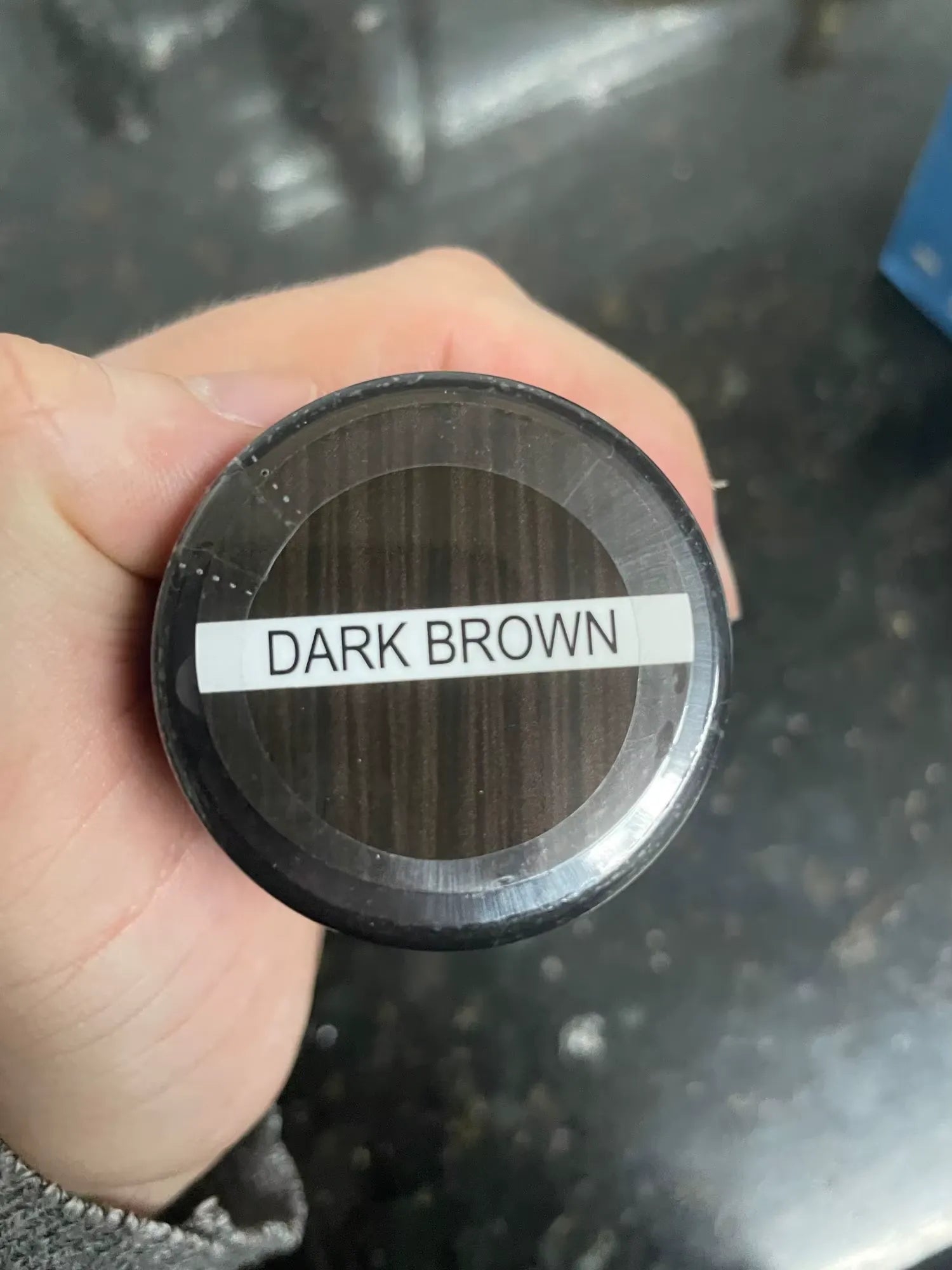 A base de um recipiente é mostrada em close, com a identificação de tonalidade Dark Brown.